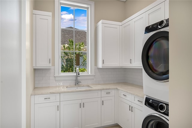 clothes washing area with cabinets, stacked washing maching and dryer, sink, and a wealth of natural light