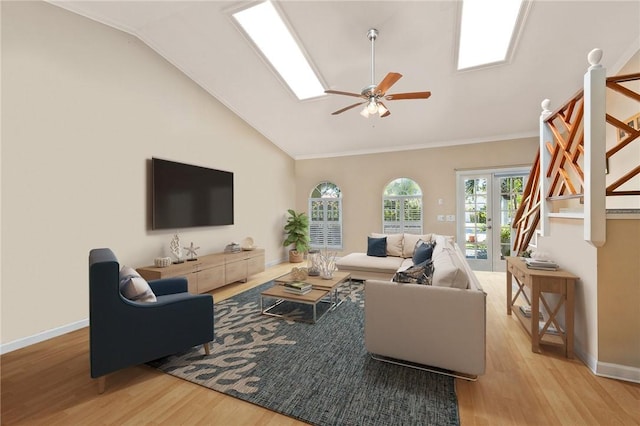 living room with ceiling fan, vaulted ceiling with skylight, crown molding, light hardwood / wood-style flooring, and french doors