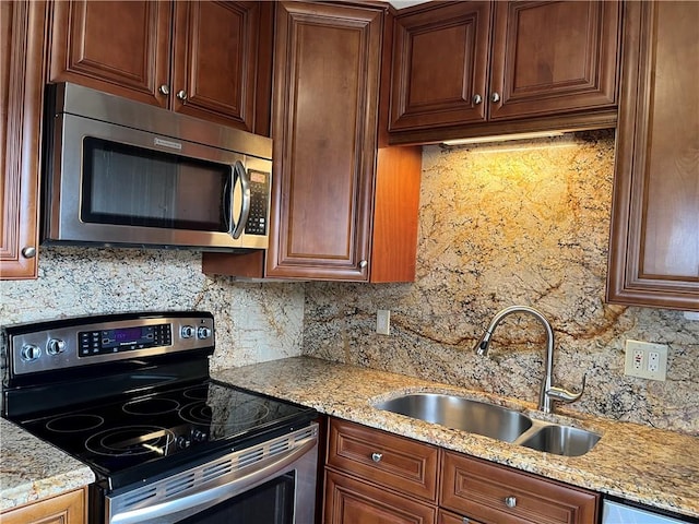 kitchen featuring light stone countertops, appliances with stainless steel finishes, backsplash, and a sink