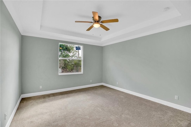 empty room with a tray ceiling, ceiling fan, and carpet flooring