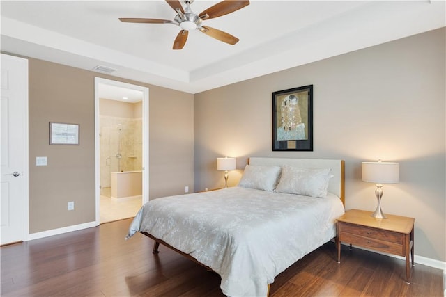 bedroom with dark wood-type flooring, ceiling fan, connected bathroom, and a raised ceiling