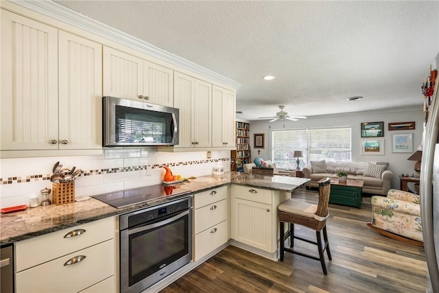 kitchen with kitchen peninsula, appliances with stainless steel finishes, dark hardwood / wood-style flooring, a breakfast bar, and cream cabinets