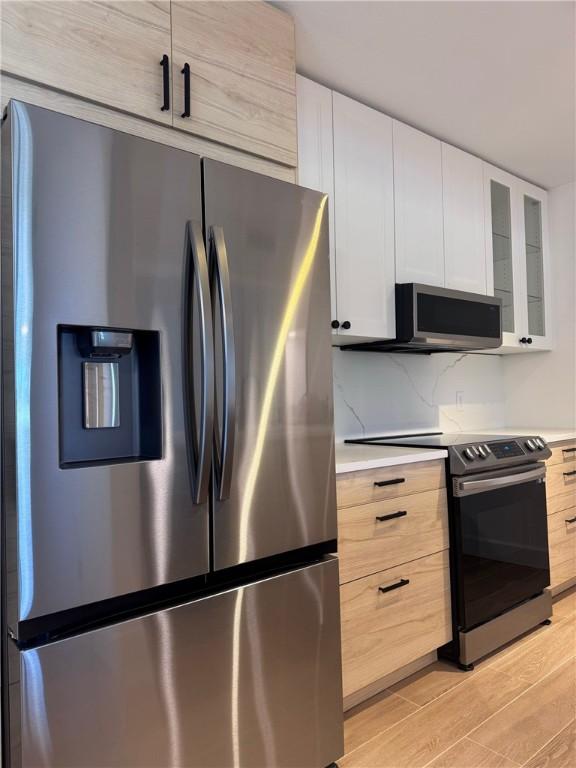 kitchen with light wood finished floors, light countertops, appliances with stainless steel finishes, glass insert cabinets, and white cabinets