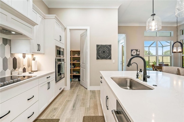 kitchen with a sink, stainless steel appliances, light countertops, light wood-style floors, and crown molding