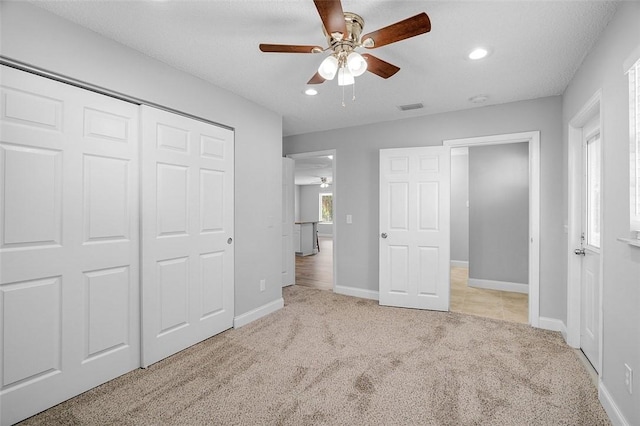 unfurnished bedroom with ceiling fan, a textured ceiling, light carpet, and a closet