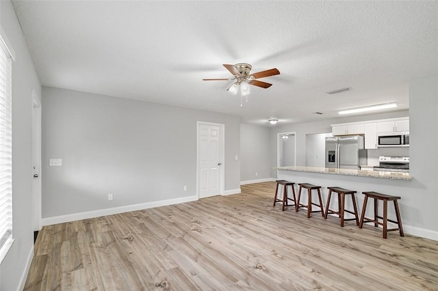 kitchen with appliances with stainless steel finishes, ceiling fan, light wood-type flooring, and a textured ceiling