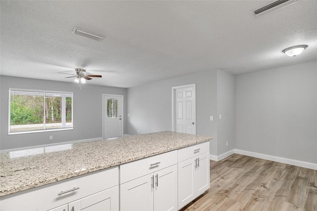 kitchen featuring a textured ceiling, light hardwood / wood-style floors, white cabinets, and light stone counters