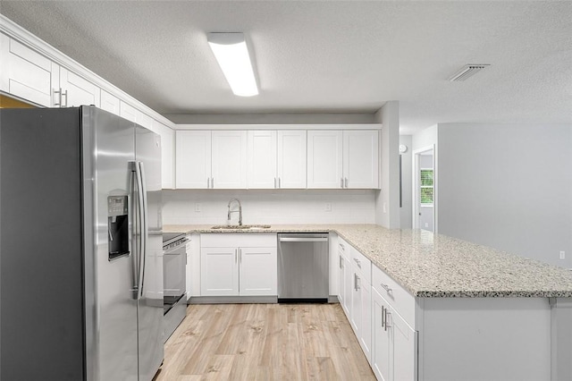 kitchen featuring white cabinetry, kitchen peninsula, stainless steel appliances, light stone countertops, and sink