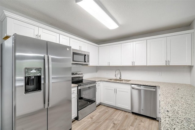 kitchen with stainless steel appliances, light stone countertops, light hardwood / wood-style floors, sink, and white cabinets