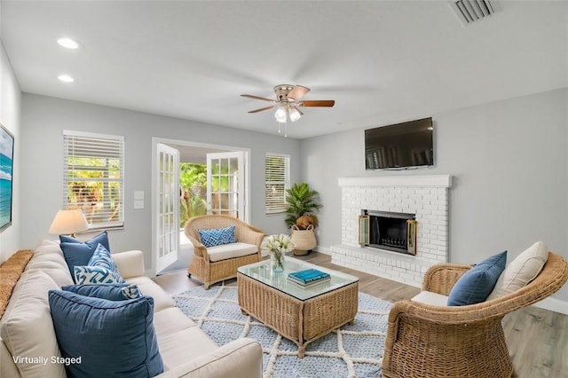 living room featuring light hardwood / wood-style flooring, ceiling fan, and a fireplace