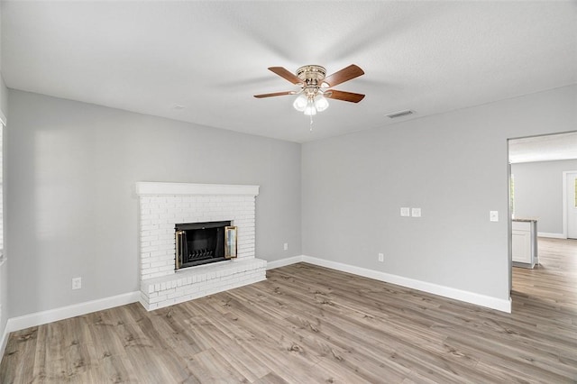 unfurnished living room featuring a brick fireplace, ceiling fan, and light hardwood / wood-style flooring