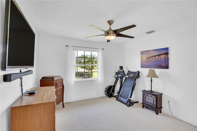 workout area with light carpet, ceiling fan, and a wood stove