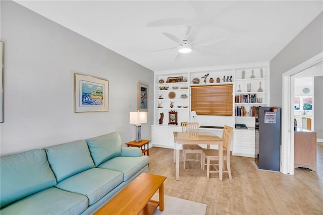 living room featuring built in shelves, ceiling fan, and light hardwood / wood-style floors