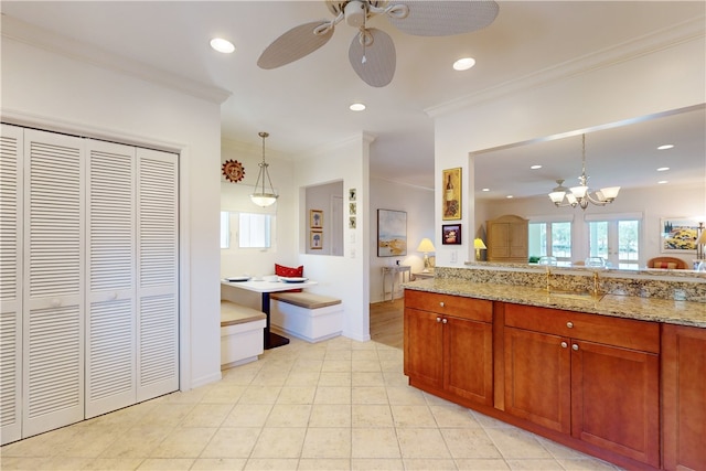 kitchen with light tile patterned flooring, crown molding, light stone countertops, pendant lighting, and ceiling fan with notable chandelier