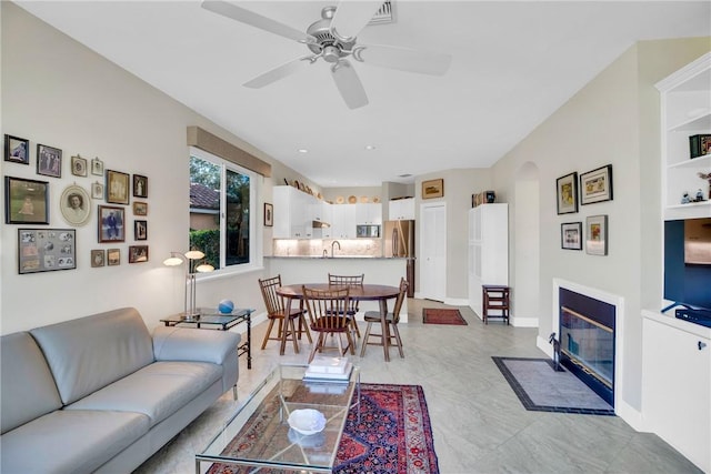 living area with ceiling fan, arched walkways, a fireplace with flush hearth, and baseboards