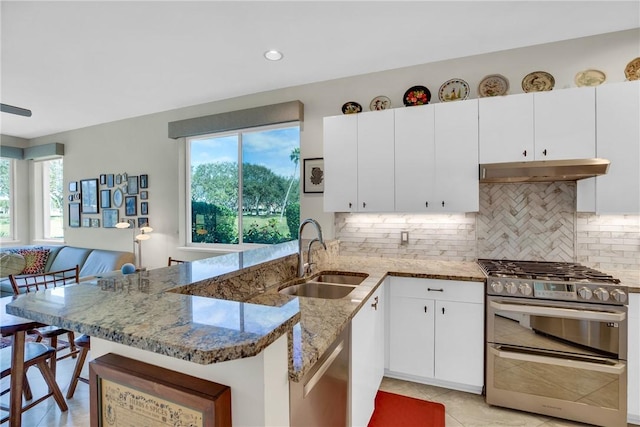 kitchen with under cabinet range hood, stainless steel appliances, a peninsula, a sink, and backsplash