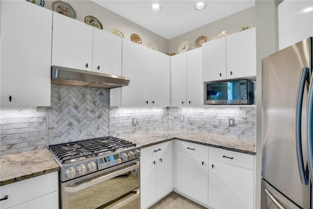 kitchen with under cabinet range hood, stone counters, appliances with stainless steel finishes, and backsplash