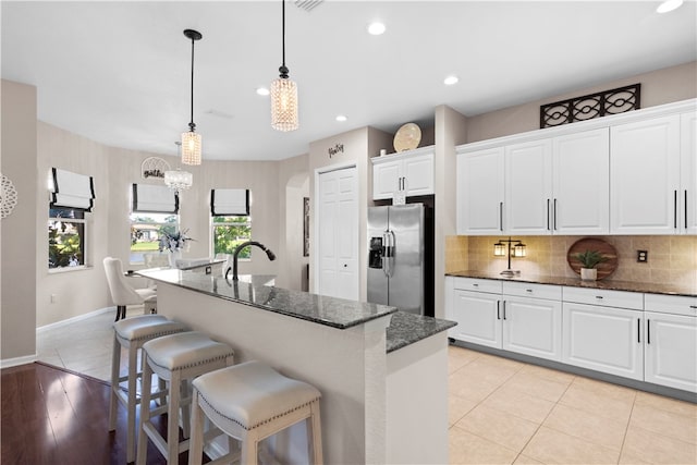 kitchen featuring stainless steel fridge, a kitchen bar, decorative backsplash, an island with sink, and white cabinets