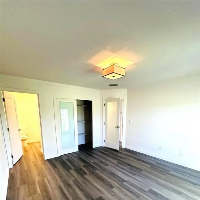 unfurnished bedroom with ensuite bathroom, a closet, and dark wood-type flooring