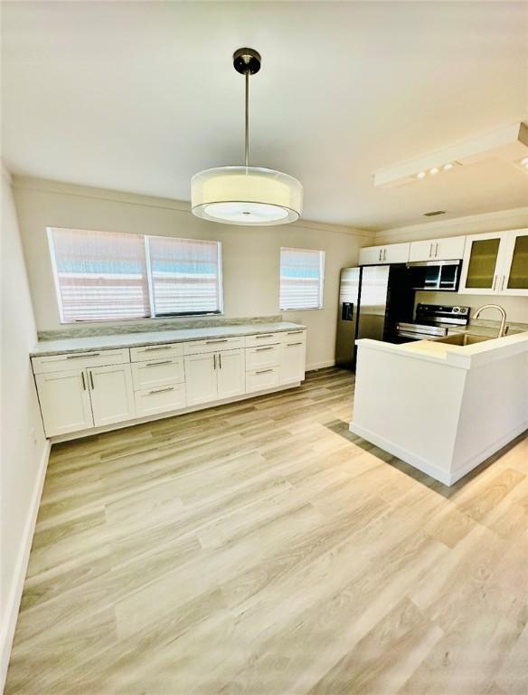 kitchen featuring appliances with stainless steel finishes, decorative light fixtures, white cabinetry, and light hardwood / wood-style flooring