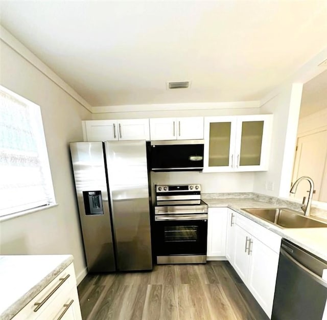 kitchen with wood-type flooring, appliances with stainless steel finishes, sink, and white cabinetry