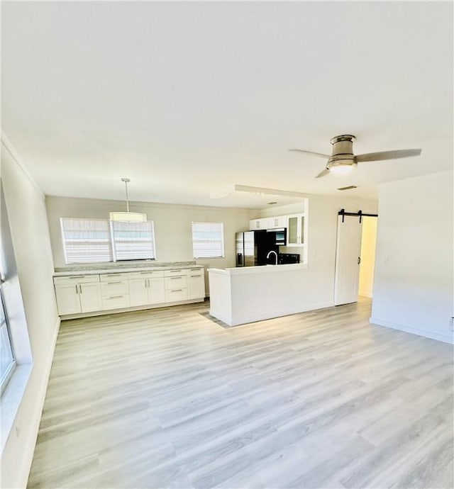 unfurnished living room with ceiling fan, a barn door, and light wood-type flooring