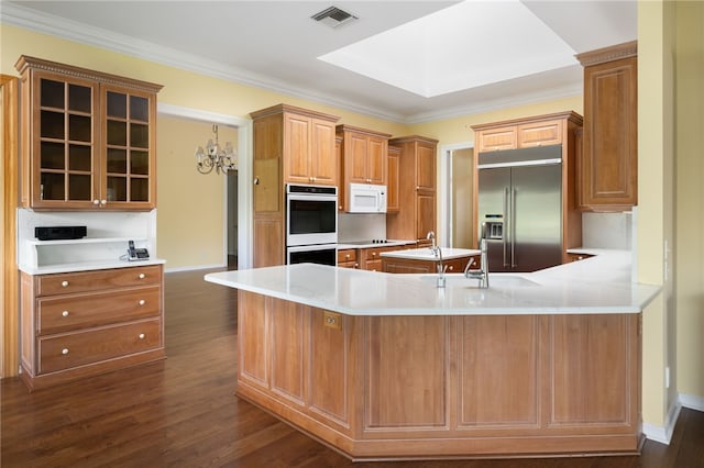 kitchen featuring stainless steel appliances, kitchen peninsula, ornamental molding, an inviting chandelier, and dark wood-type flooring