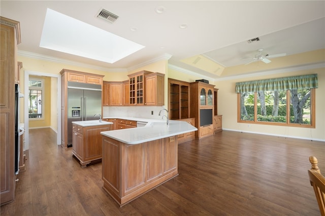 kitchen featuring built in refrigerator, kitchen peninsula, ceiling fan, dark hardwood / wood-style floors, and a skylight