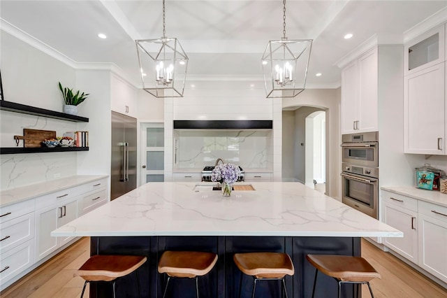 kitchen with stainless steel appliances, a center island with sink, white cabinetry, a breakfast bar, and light stone countertops