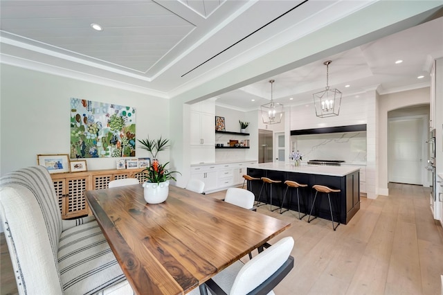 dining area with light hardwood / wood-style floors, ornamental molding, a raised ceiling, and a notable chandelier