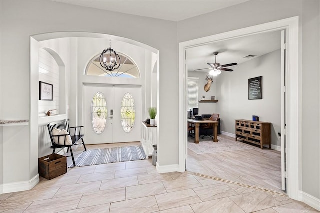 tiled foyer entrance featuring french doors and ceiling fan with notable chandelier