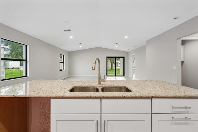 kitchen featuring light stone countertops, white cabinetry, lofted ceiling, and sink