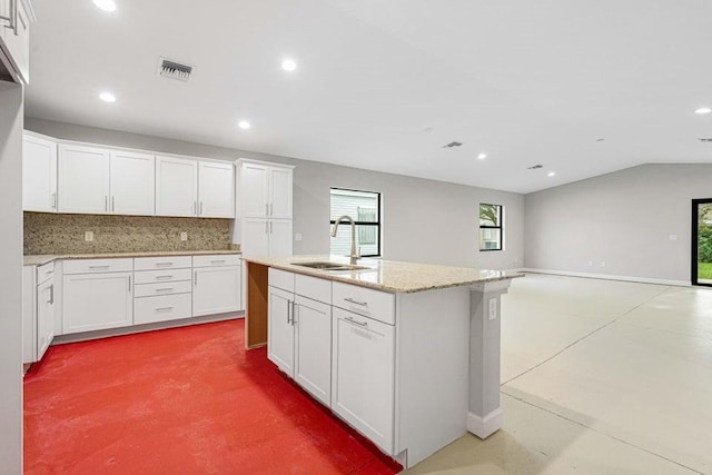 kitchen featuring white cabinetry, sink, light stone countertops, tasteful backsplash, and an island with sink