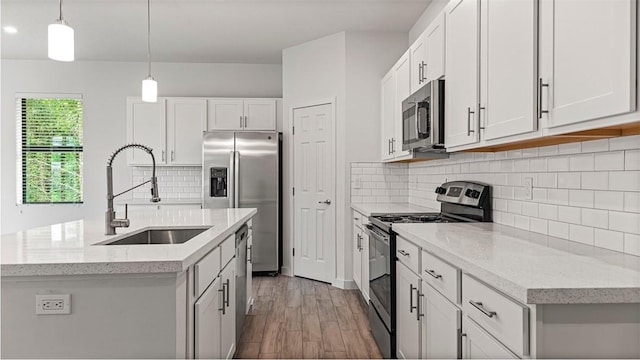 kitchen featuring hanging light fixtures, sink, an island with sink, appliances with stainless steel finishes, and white cabinetry