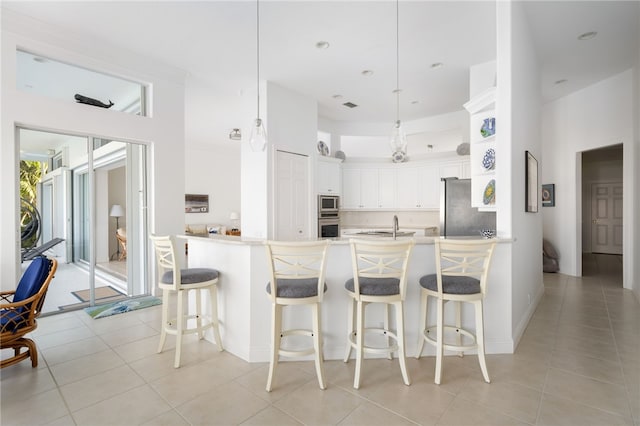 kitchen featuring kitchen peninsula, decorative light fixtures, light tile patterned flooring, white cabinetry, and stainless steel appliances