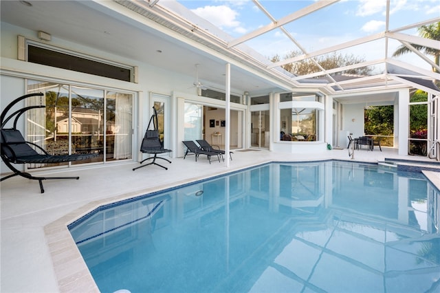 view of swimming pool featuring glass enclosure, ceiling fan, and a patio