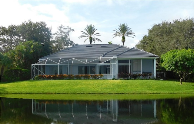 rear view of house with glass enclosure, a yard, and a water view