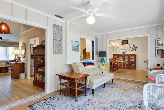 tiled living room with ceiling fan with notable chandelier and ornamental molding