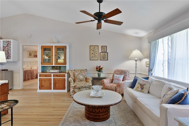 living room with ceiling fan, light wood-type flooring, and vaulted ceiling