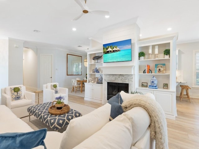 living room featuring a premium fireplace, ornamental molding, ceiling fan, and light hardwood / wood-style floors