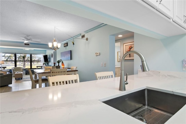 kitchen with a sink, open floor plan, white cabinets, tile patterned flooring, and hanging light fixtures