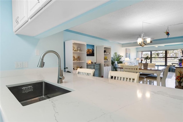 kitchen with light stone counters, a sink, hanging light fixtures, white cabinetry, and open floor plan