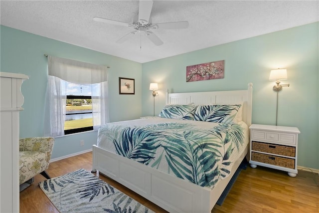 bedroom with ceiling fan, a textured ceiling, baseboards, and wood finished floors