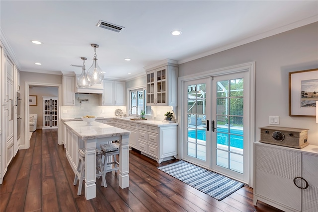 kitchen featuring french doors, white cabinetry, a center island, hanging light fixtures, and decorative backsplash