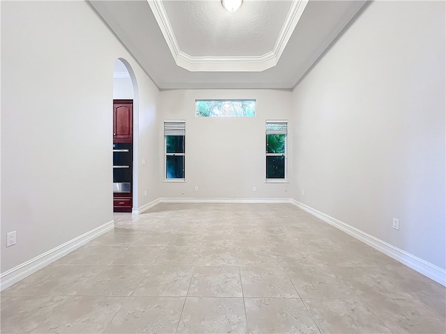 spare room with arched walkways, a textured ceiling, baseboards, a raised ceiling, and crown molding