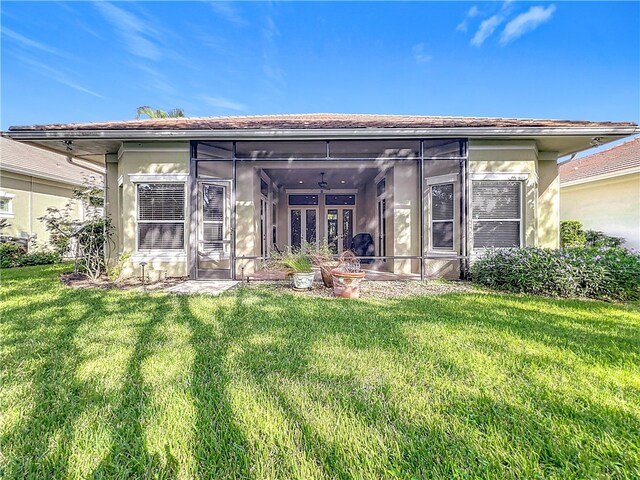 rear view of house featuring a sunroom, a lawn, and stucco siding