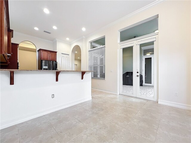 1237 River Reach Dr, Vero Beach, FL 32967 - kitchen featuring black fridge with ice dispenser, a breakfast bar area, arched walkways, crown molding, and baseboards
