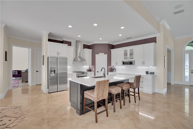 kitchen featuring ornamental molding, white cabinetry, wall chimney range hood, appliances with stainless steel finishes, and sink