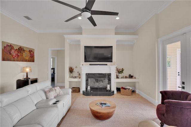 living room featuring light carpet, a tiled fireplace, ceiling fan, and ornamental molding