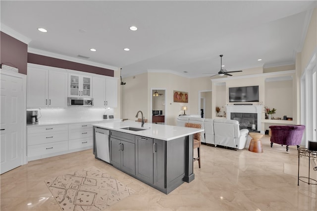 kitchen with stainless steel appliances, sink, ornamental molding, a kitchen island with sink, and white cabinets